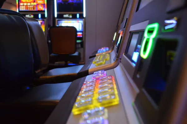 A close-up, angled view of a row of modern slot machines in a casino, showing the illuminated buttons and screens, with other machines visible in the background, creating a vibrant and engaging atmosphere.