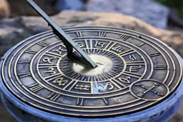 A close-up of an ornate brass sundial with Roman numerals and zodiac symbols, casting a shadow to indicate time.