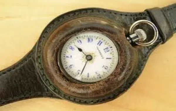 A vintage pocket watch converted into a wristwatch with a worn brown leather strap, showing a white face with blue numerals.