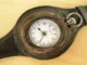 A vintage pocket watch converted into a wristwatch with a worn brown leather strap, showing a white face with blue numerals.