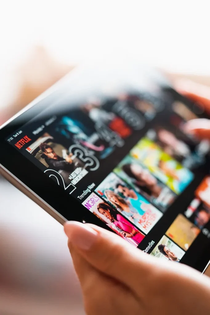 Close-up of hands holding a tablet displaying the Netflix interface with various movie and TV show titles.