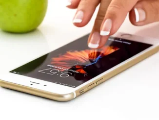 A hand with well-manicured nails touching the screen of a gold smartphone displaying a vibrant abstract wallpaper and the time.