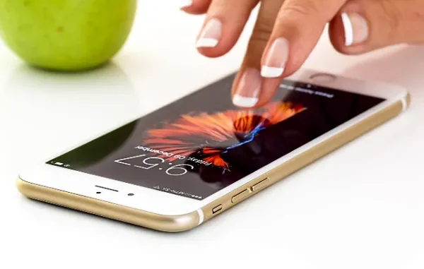 Engaging with Mobile Apps A hand with well-manicured nails touching the screen of a gold smartphone displaying a vibrant abstract wallpaper and the time.