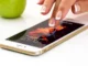 A hand with well-manicured nails touching the screen of a gold smartphone displaying a vibrant abstract wallpaper and the time.