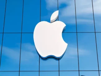 The iconic white Apple logo prominently displayed on the exterior of a modern glass building, reflecting a blue sky.