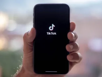 A hand holding a modern smartphone with the TikTok logo and name displayed on a black screen, symbolizing a platform where viral trends and keywords originate.