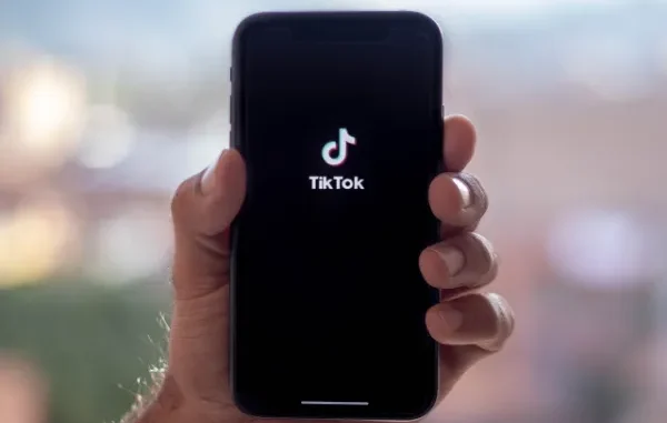 The Source of Virality: Social Media Trend Discovery A hand holding a modern smartphone with the TikTok logo and name displayed on a black screen, symbolizing a platform where viral trends and keywords originate.