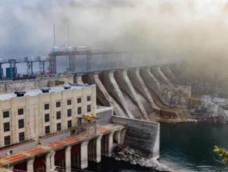 A massive hydroelectric dam with a large, concrete retaining wall holding back a vast reservoir of deep blue water, symbolizing critical, resilient infrastructure and community water security.
