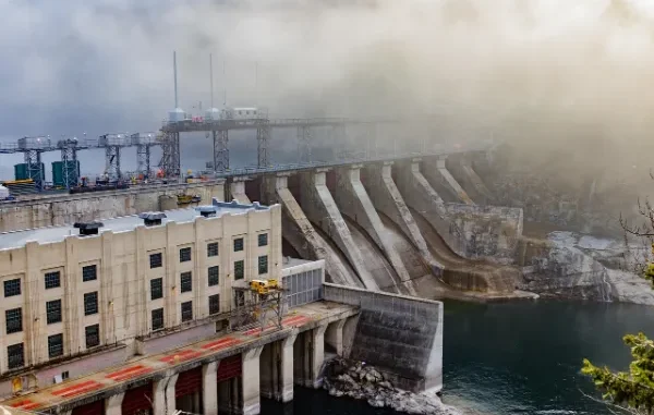 A massive hydroelectric dam with a large, concrete retaining wall holding back a vast reservoir of deep blue water, symbolizing critical, resilient infrastructure and community water security.