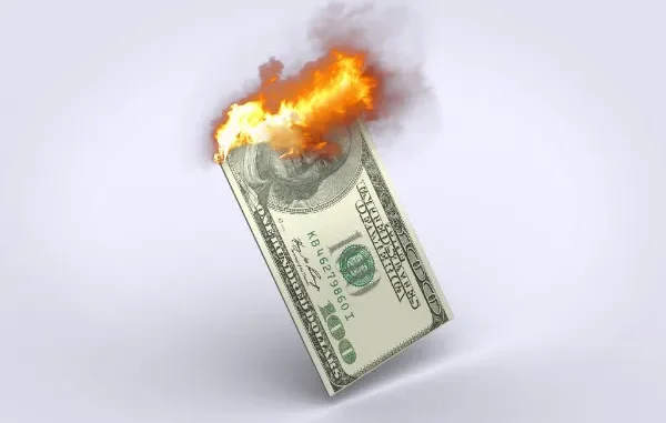Burning US dollar bill symbolizing inflation eroding purchasing power and causing financial stress.